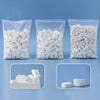 Several clear plastic bags filled with white compressed camping towels and loose towels.