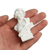 A white plaster bust miniature of a classical Greek goddess, held in a person's hand.