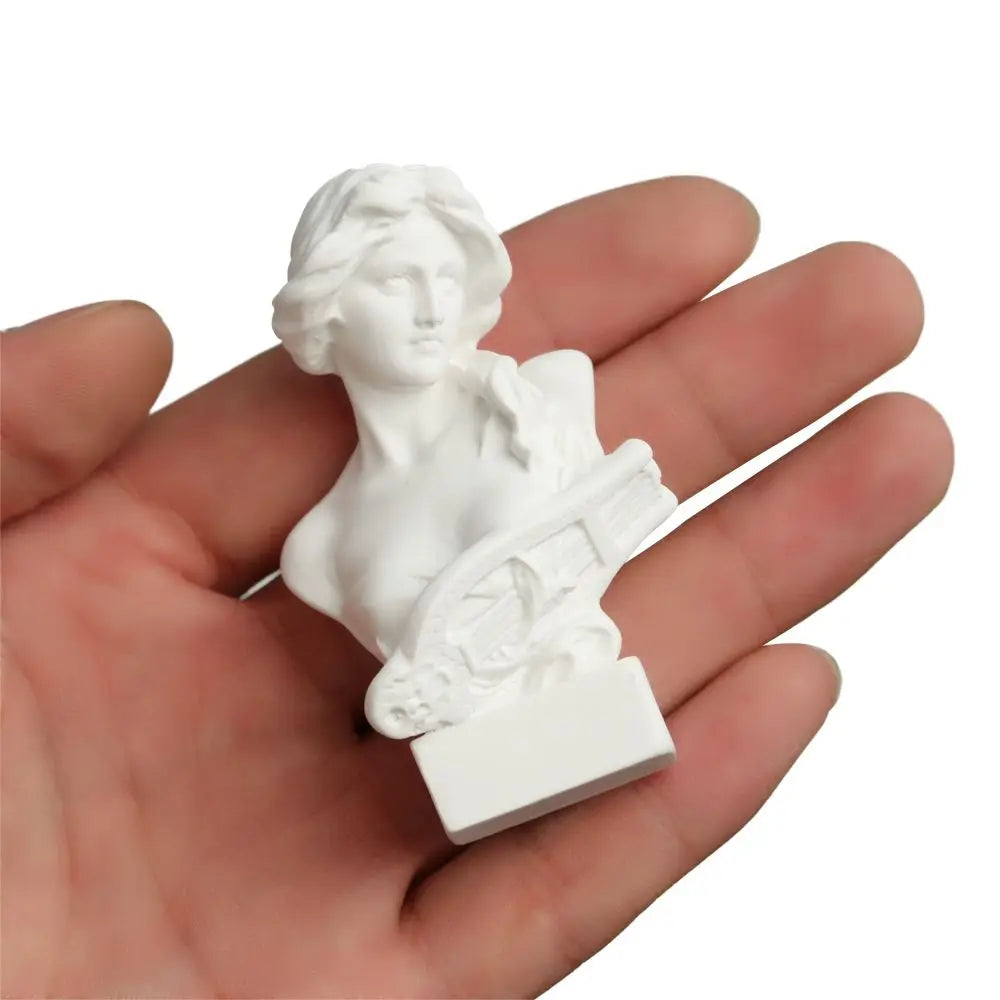 A white plaster bust miniature of a classical Greek goddess, held in a person's hand.