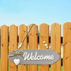 A wooden welcome sign with the word Welcome hanging on a wooden fence.