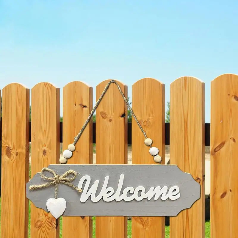 A wooden welcome sign with the word Welcome hanging on a wooden fence.
