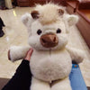 A fluffy white Highland cow plush toy with brown accents being held by a person.