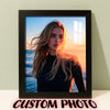A framed photo of a woman with long blonde hair looking towards the sunset, set against a blue ocean background.