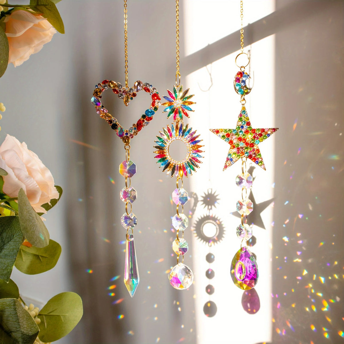 A collection of crystal rainbow sun catchers featuring heart, star, and circle designs hanging against a bright background.