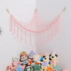 Pink cotton hammock toy for stuffed animals and plushies hanging on a white wall