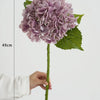 A cluster of purple hydrangea silk flowers on a green stem, shown next to a ruler for scale.