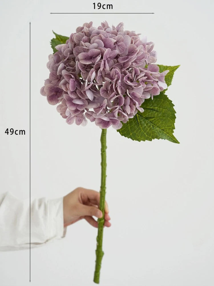 A cluster of purple hydrangea silk flowers on a green stem, shown next to a ruler for scale.