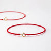 A handmade red string bracelet with a gold plated clasp lying on a white surface.