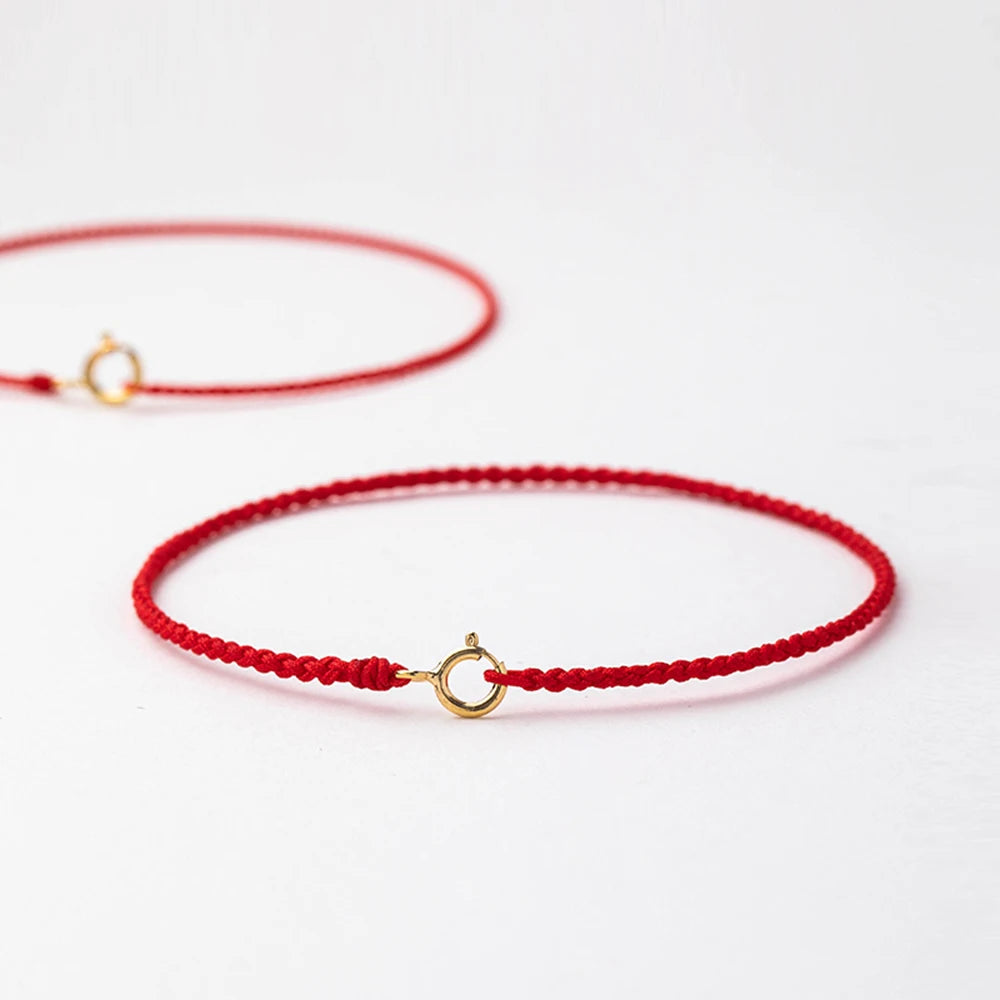 A handmade red string bracelet with a gold plated clasp lying on a white surface.