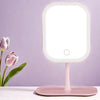 A pink smart LED makeup vanity mirror with a round light and stand on a white surface.