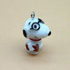 A white ceramic dog pendant with black eyes and a red collar, featuring a brown rectangular item.