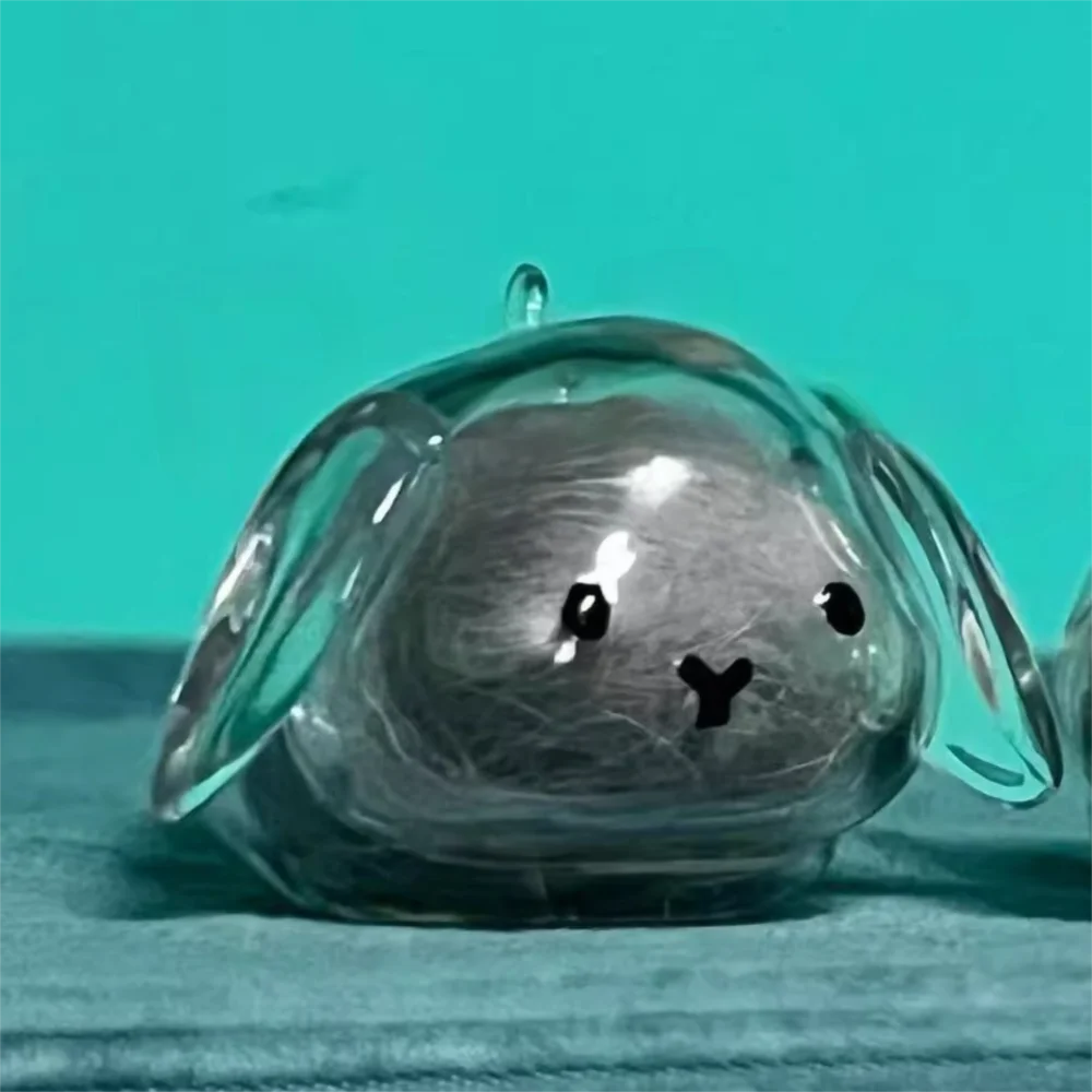 A clear glass keepsake shaped like a rabbit head with gray hair inside, resting on a blue surface.