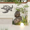 Black metal sea turtle wall art mounted on a light-colored wall with natural rocks and greenery.