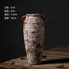 A tall, mottled ceramic flower vase with an antique finish sits on a wooden surface.