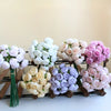 A collection of silk peony bouquets in shades of white, pink, and purple arranged on a wooden rack.