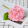 A pink artificial hydrangea flower cluster resting on a white background with a black grid pattern.