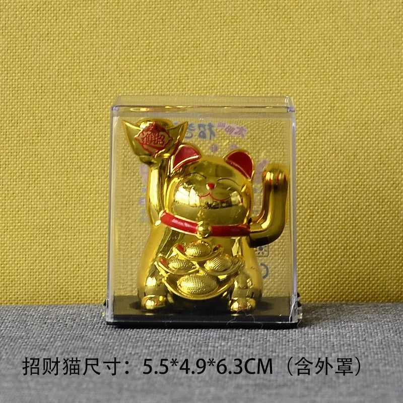 A gold-colored solar-powered waving lucky cat figurine displayed in a clear plastic case.