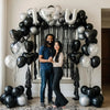 Arche de ballons noir et argent avec des ballons en forme de cœur et une toile de fond en guirlande noire.