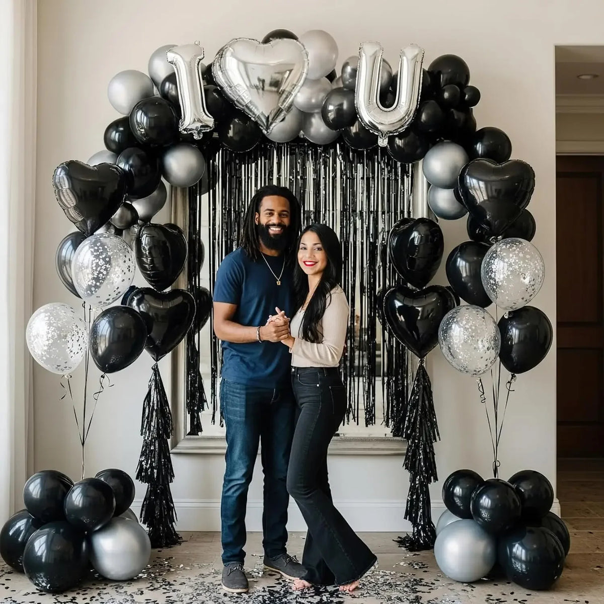 Arche de ballons noir et argent avec des ballons en forme de cœur et une toile de fond en guirlande noire.