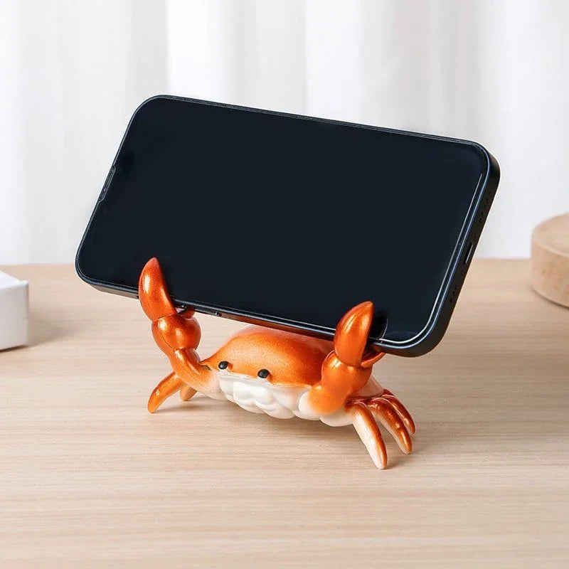 An orange crab-shaped desk organizer holding a black smartphone.
