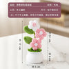 A hand-woven crochet pink and white flower arrangement potted in a white ceramic container.
