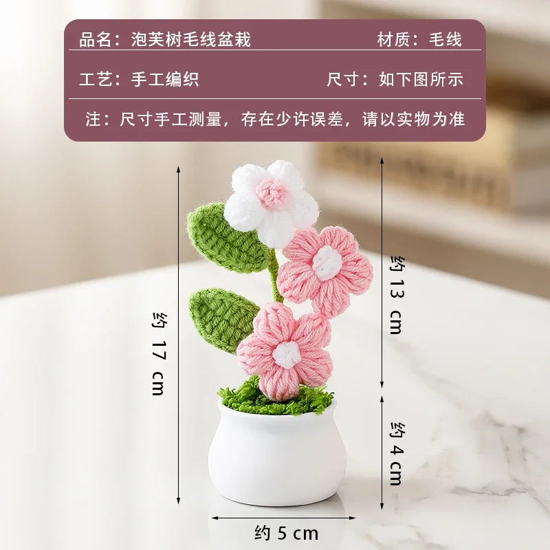 A hand-woven crochet pink and white flower arrangement potted in a white ceramic container.