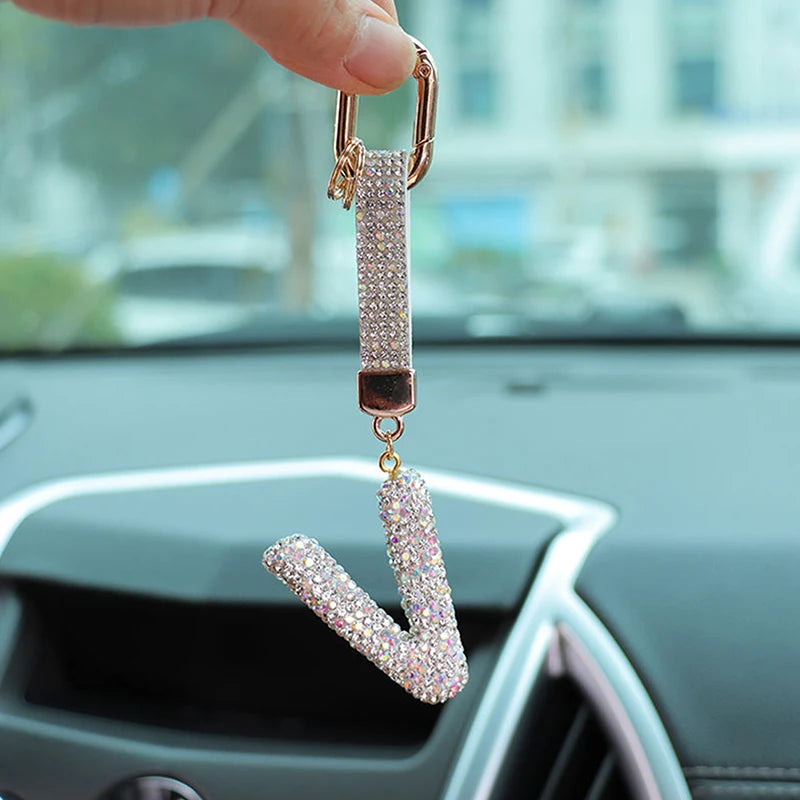 A hand holds a crystal letter keychain charm shaped like the letter I.