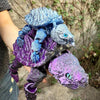 A hand holds a 3D printed alligator snapping turtle figurine with articulated joints in purple and blue colors.