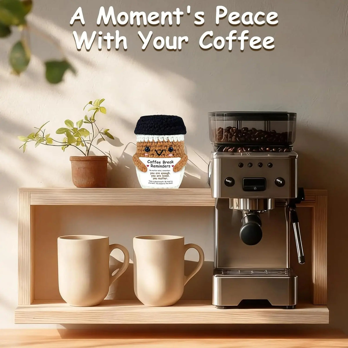 A handwoven knitted coffee cup cozy with a smiling doll decoration sits next to a coffee grinder and a mug on a wooden shelf.