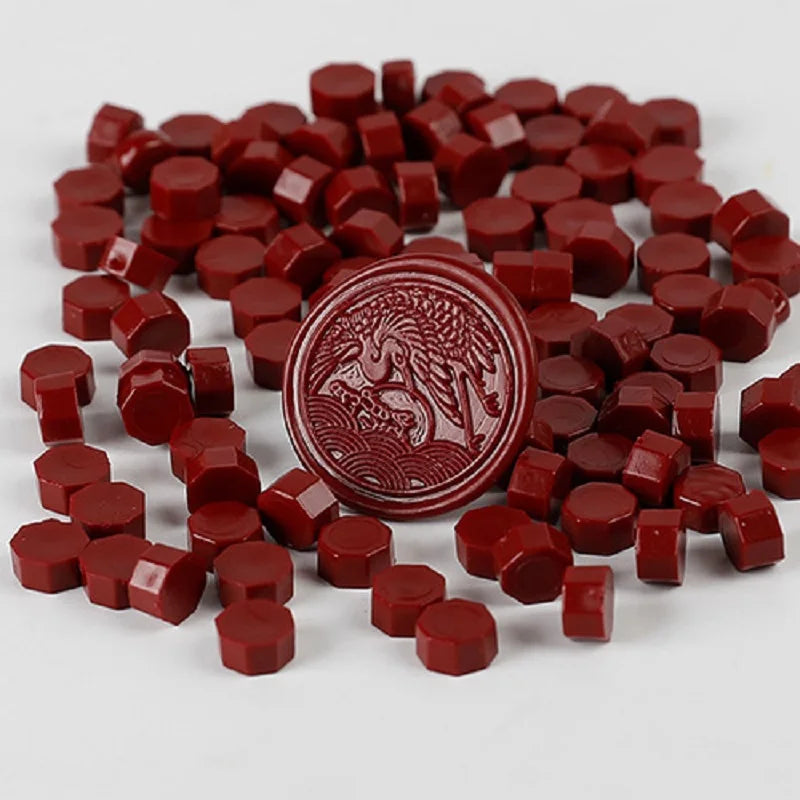 A pile of red wax sealing beads and a circular stamp impression are shown on a white background.