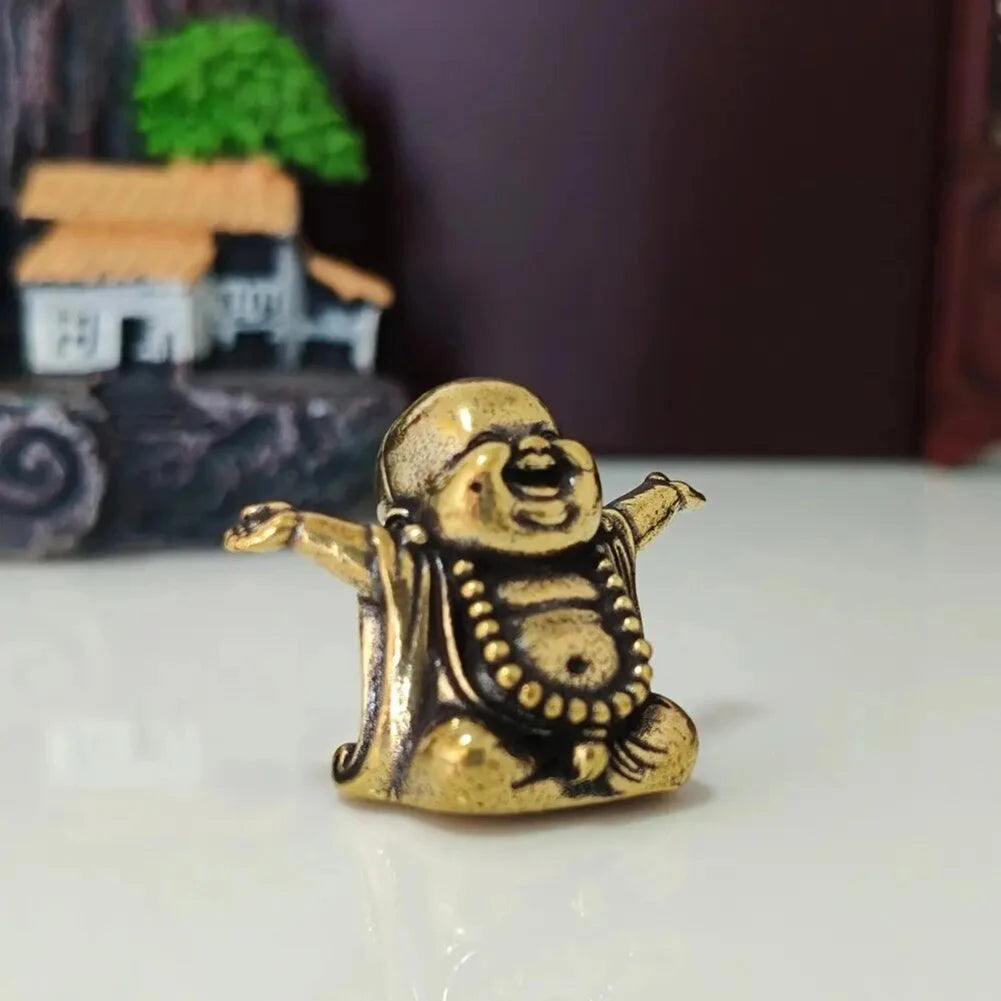 A small brass statue of a laughing Buddha with expressive features, placed on a white surface.