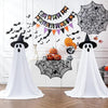 A white ghost decoration with a pointed hat is displayed against a white wall decorated with Halloween banners and spiderwebs