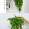 A long, green artificial ivy vine garland is displayed against a white wall, showing its texture and length.