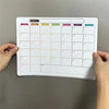A magnetic fridge planner grid showing days of the week for monthly planning with empty squares.