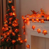 An illuminated Christmas tree decorated with orange maple leaf lights next to a white fireplace mantel adorned with more oran