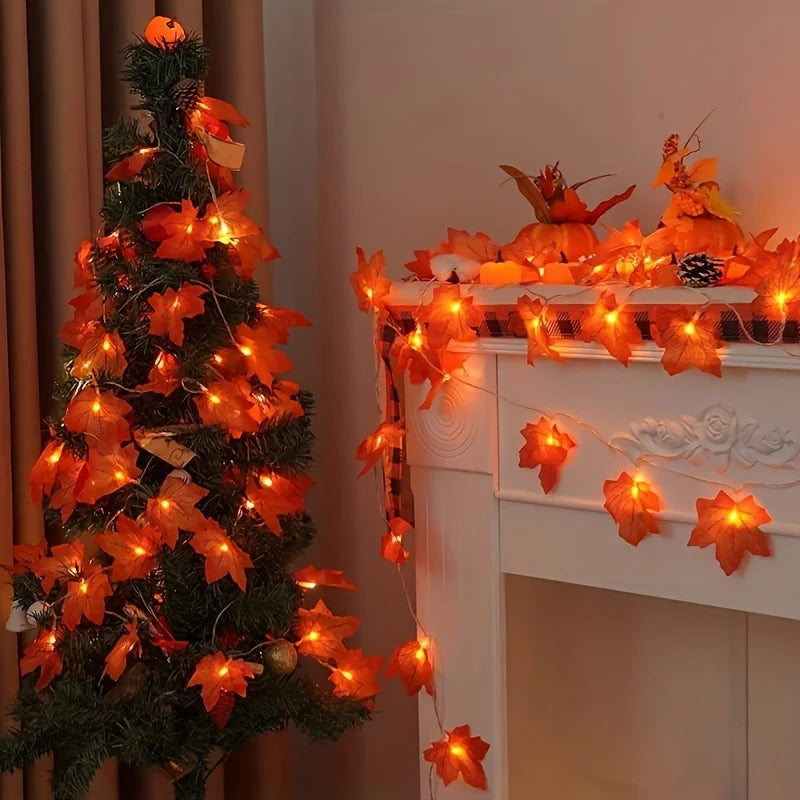 An illuminated Christmas tree decorated with orange maple leaf lights next to a white fireplace mantel adorned with more oran