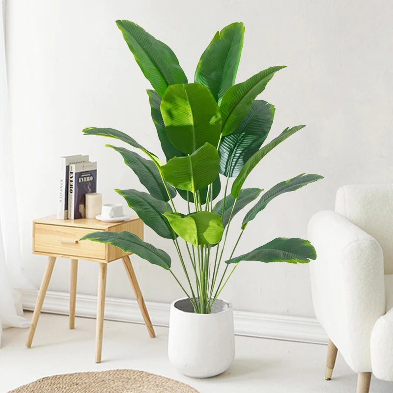 Artificial tropical palm tree with large green monstera leaves in a white pot