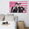 A pink American flag tapestry featuring stars and stripes, with two people posing in front of it.
