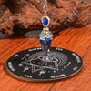 Silver pendant necklace with a blue crystal suspended over a wooden divination board