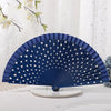 A dark blue wooden hand fan with white polka dots is displayed on a glass base.
