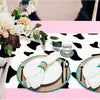 Pink cow print western tablecloth with white plates and silverware set for a party.