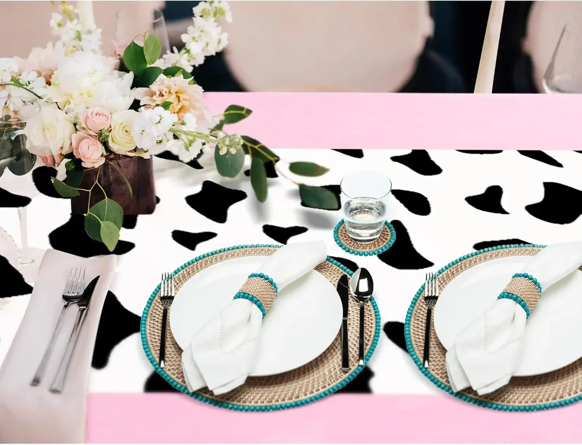 Pink cow print western tablecloth with white plates and silverware set for a party.