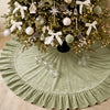 A festive velvet Christmas tree skirt with a ruffled edge decorated with white bows, ornaments, and pinecones.