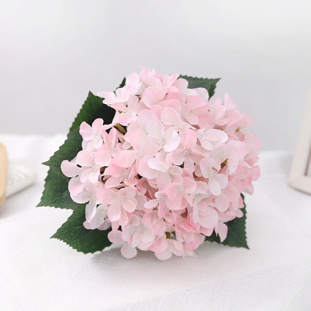 A bouquet of pink artificial hydrangea flowers resting on a white surface.