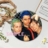 A set of collectible brooches featuring portraits of three individuals with brightly colored hair against a dark background.