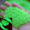 A hand holds a pile of bright, luminous green glow-in-the-dark pebbles.