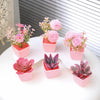 A set of six artificial potted flowers and succulents in pink and purple colors displayed on a white surface.