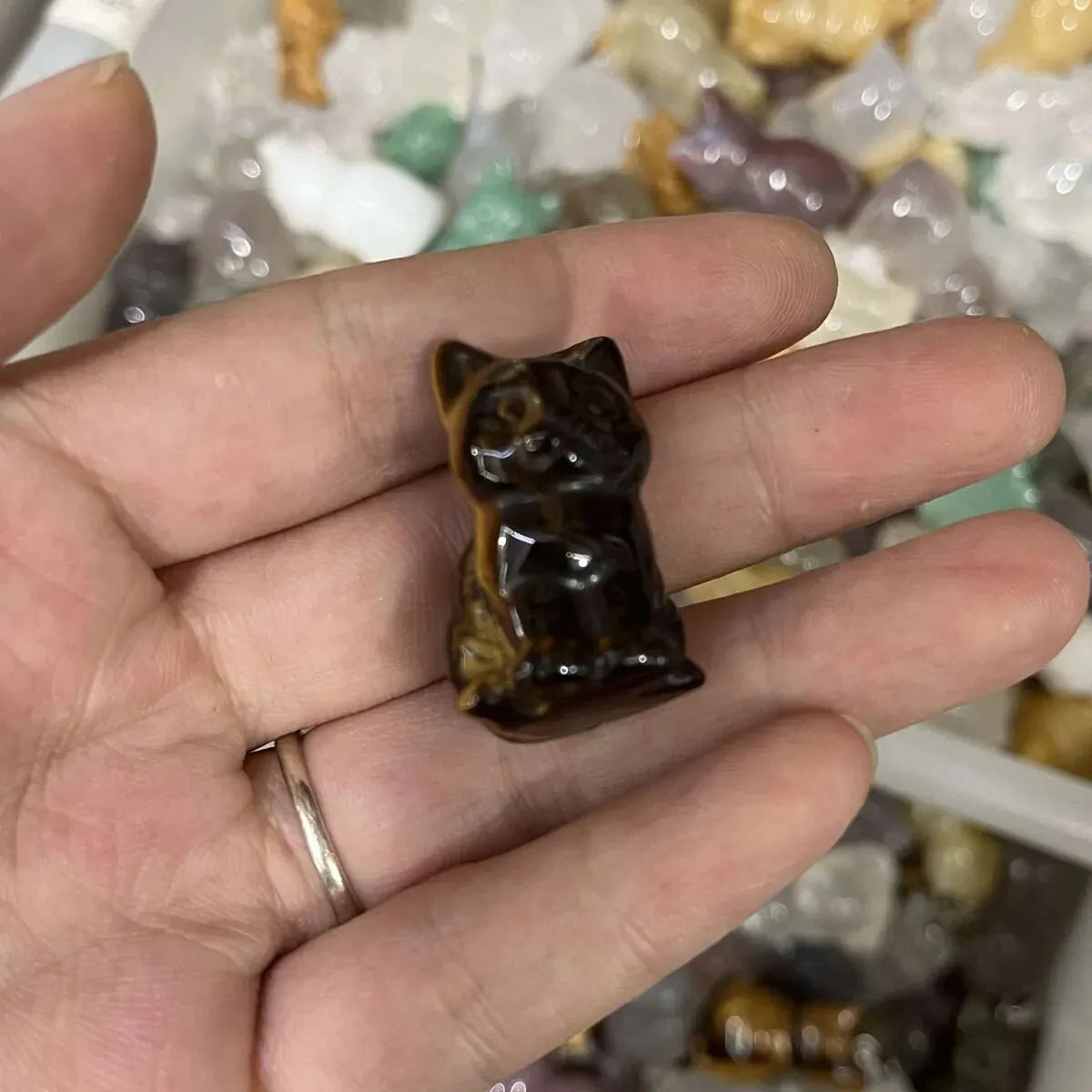 Un ornement de chat en cristal brun foncé sculpté à la main est tenu dans la paume d'une personne parmi d'autres cristaux.