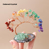 A hand holds a natural crystal tree made of various colored crystals on an agate base for home decor