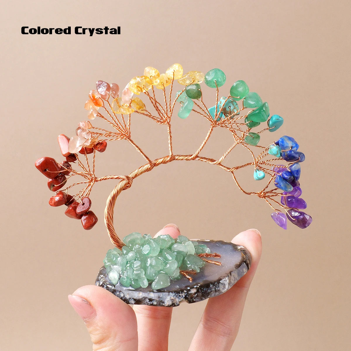 A hand holds a natural crystal tree made of various colored crystals on an agate base for home decor